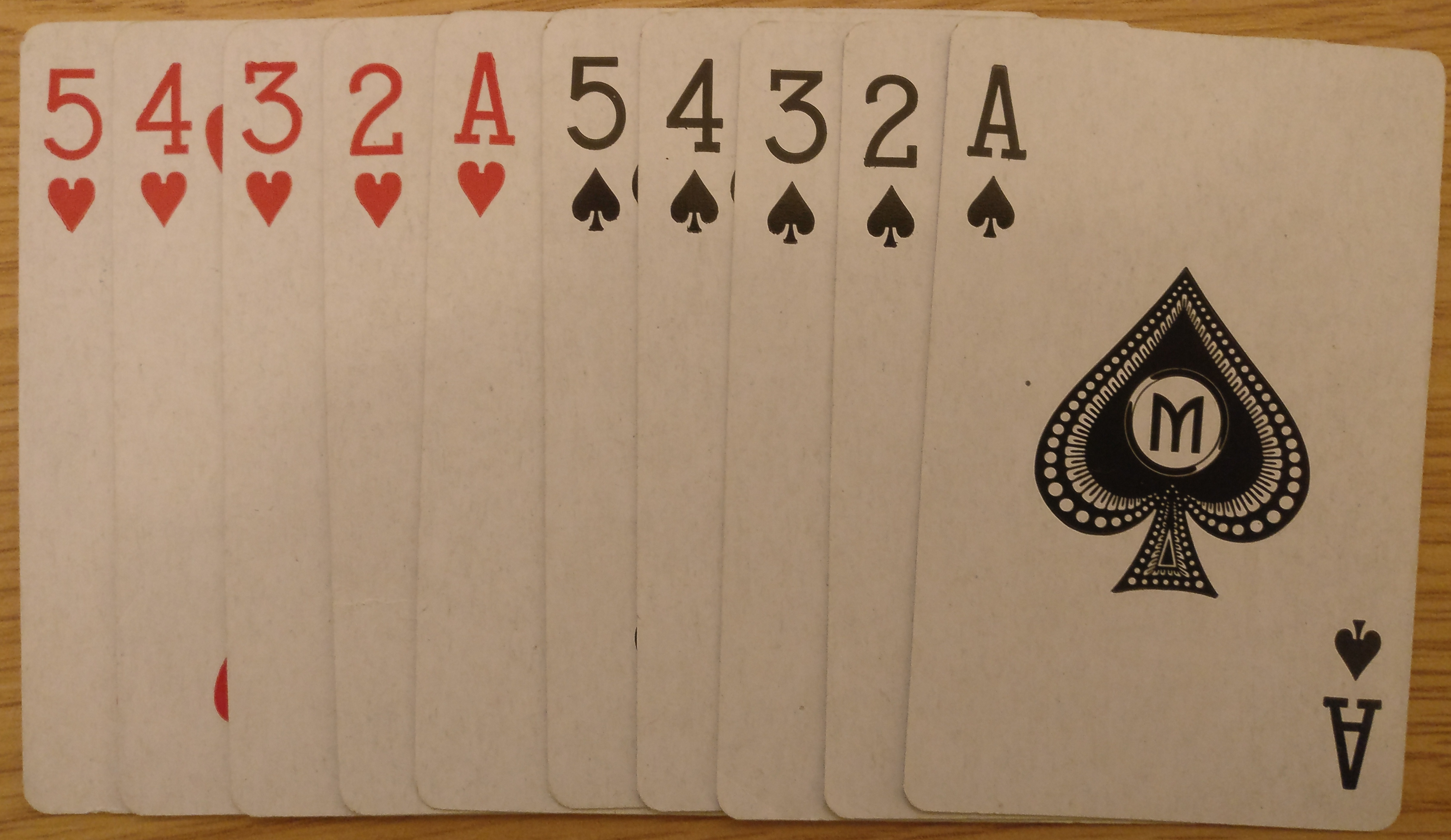 Close up of 10 playing cards are shown, 5 hearts (left) and 5 spades (right). Cards decrease from 5 to ace left to right for both suits.